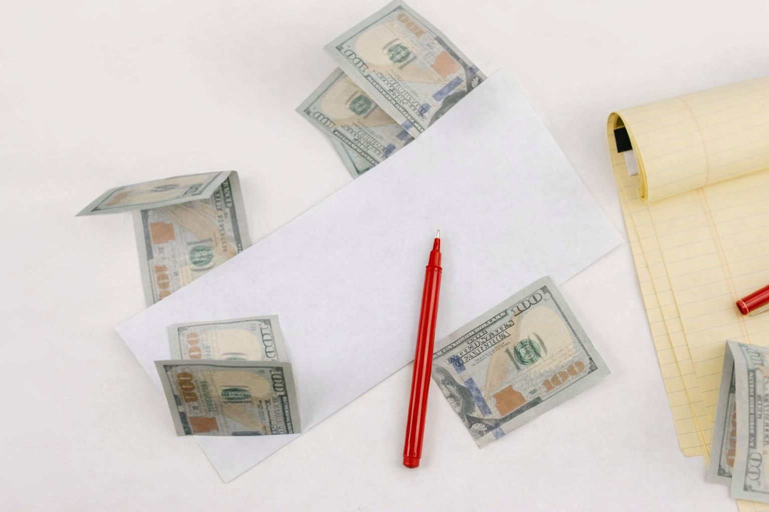 Amerikanske dollarsedler, en hvit konvolutt og en rød penn på et bord.